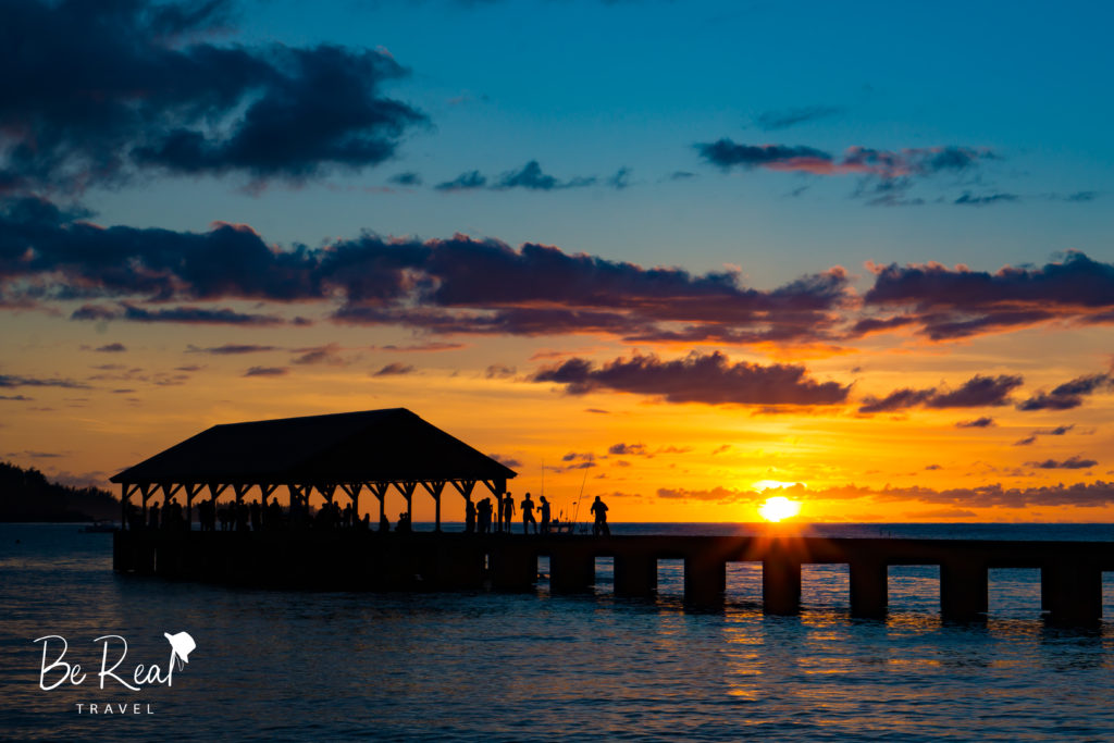 As the sun sets over the ocean, silhouettes line Hanalei Pier, Kauai, Hawaii