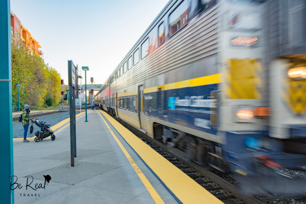 A blurred Amtrak train pulls into Emeryville station as a mother and baby look on, California