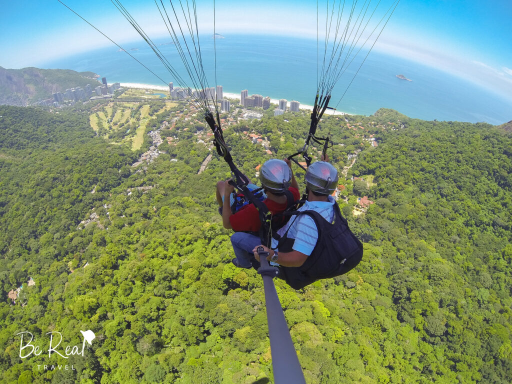 Two men paraglide over forested outskirts of Rio de Janeiro