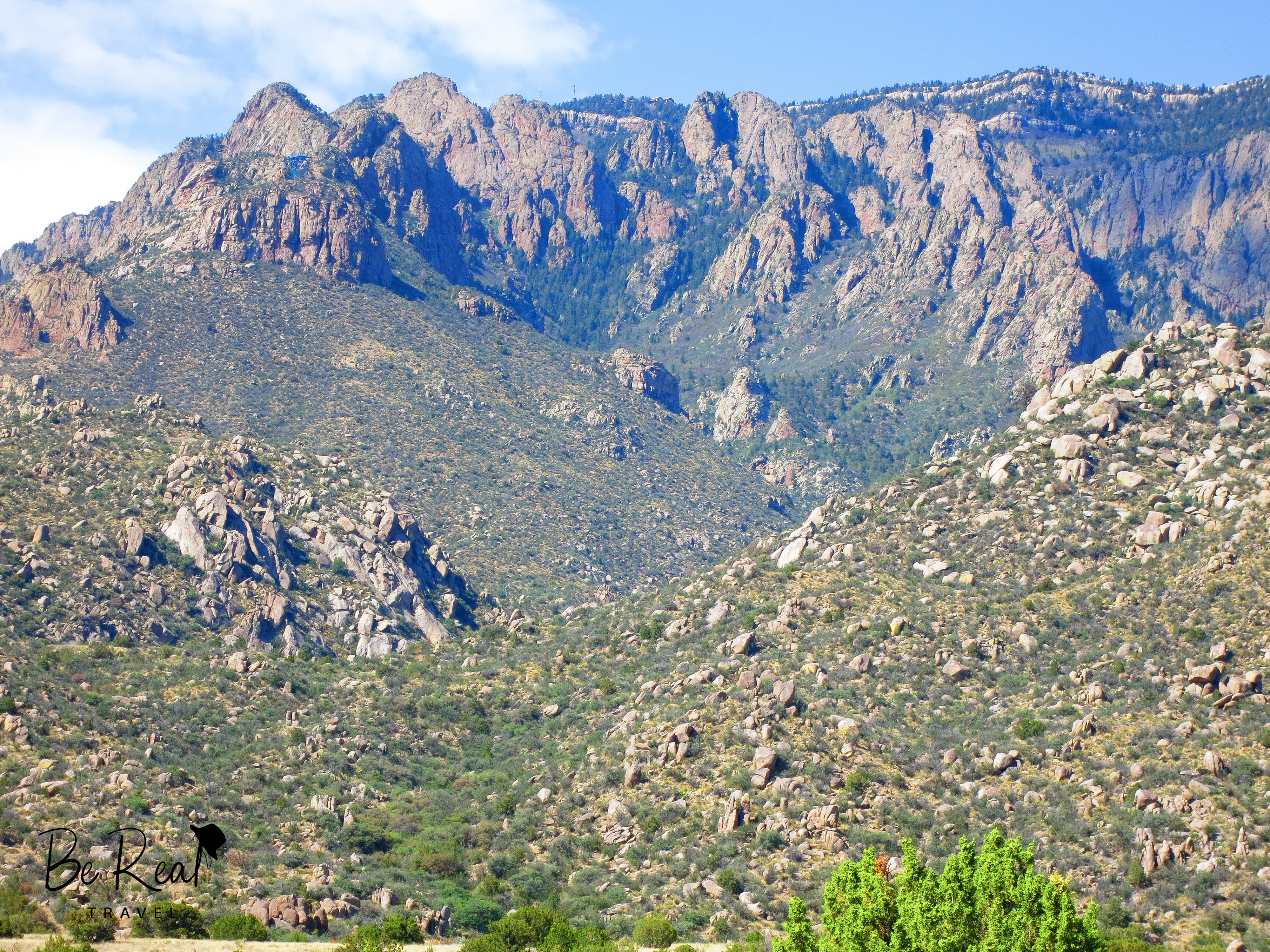 A close up of New Mexican mountains  shows rocky terrain with splashes of green sprinkled in