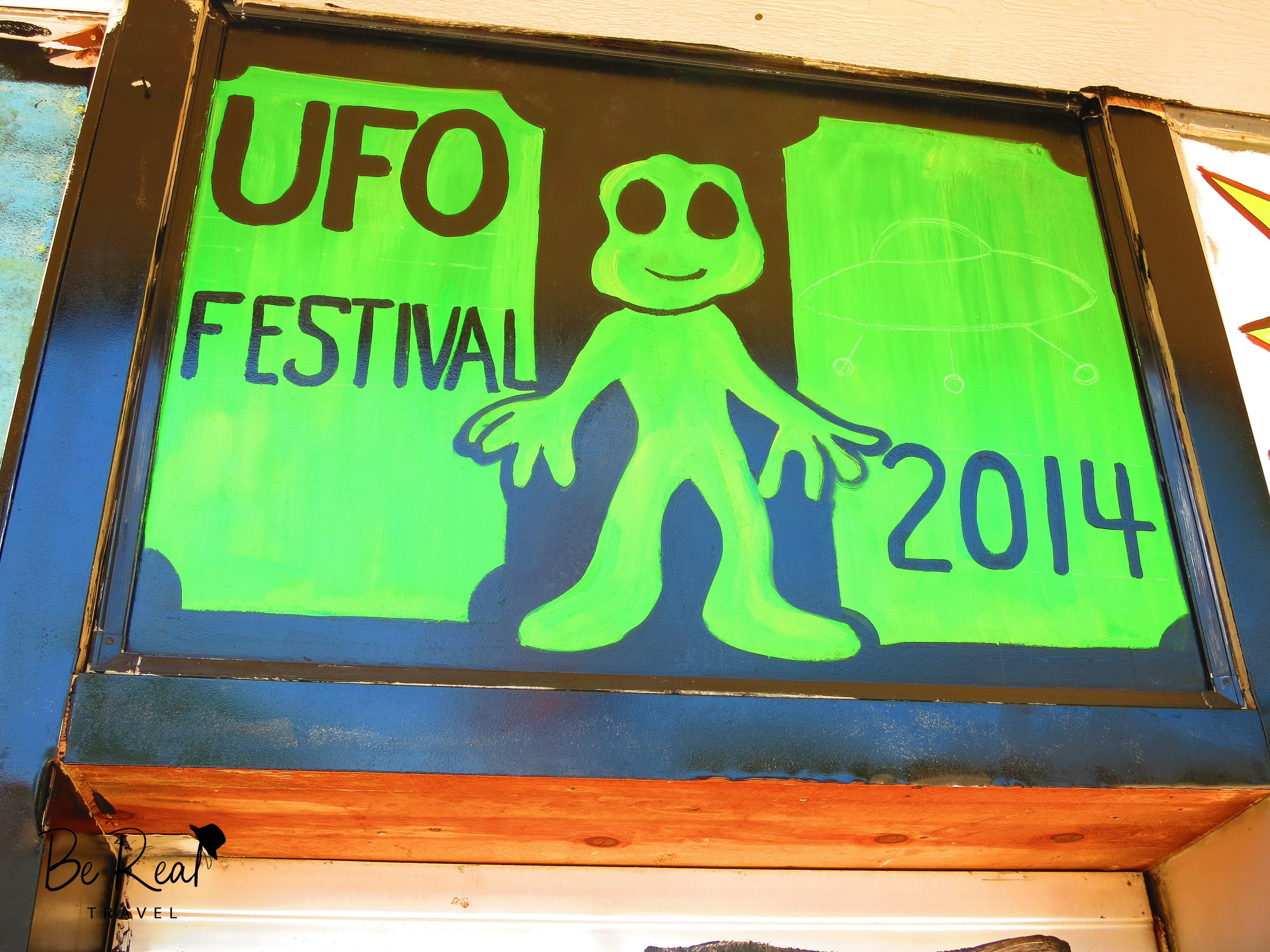 A painted sign promoting the 2014 UFO festival features a green alien in Roswell, New Mexico